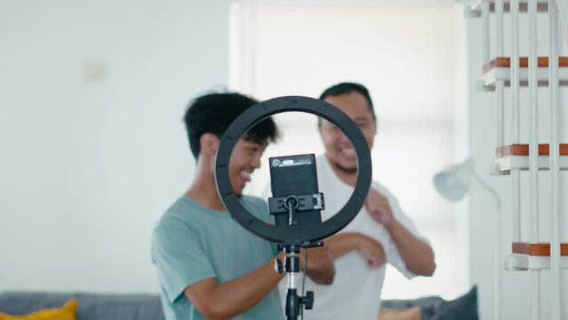 Selective Focus Smartphone and Ringlight Recording Attractive Two Young Man Dancing, Live Streaming on Social Media Platform 