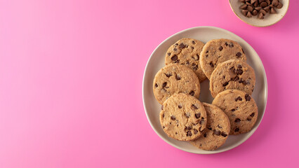 Chocolate chip cookie on a plate against a pink background. Copy space
