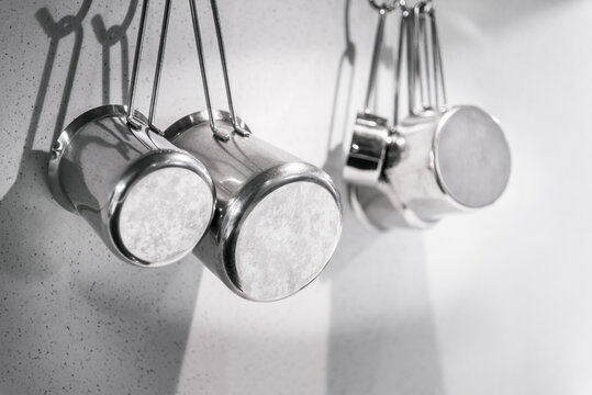 Stainless Steel Cooking Pots Hanging On A White Wall