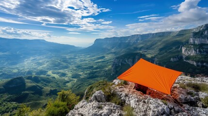 Obraz premium A compact, foldable sunshade in bright orange, set up on a rocky mountain overlook with a panoramic view of the valley below.
