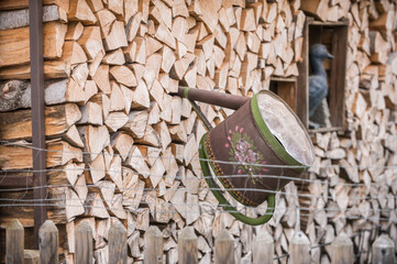 Kunstvoll bemalte Gießkanne steckt in Holzstoß
hinter Jägerzaun
