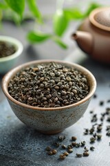 Green tea leaves in a bowl with a teapot in the background