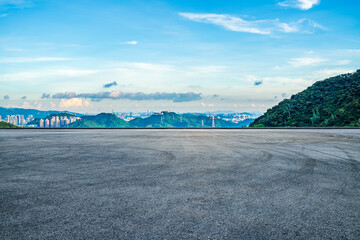 Asphalt road and green mountains with city skyline at sunrise