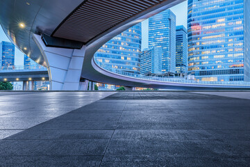 Empty square floor and pedestrian bridge with modern city buildings at dusk in Shanghai.