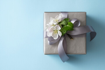 Gift box with apple flowers and gray bow on blue background. Space for your text.