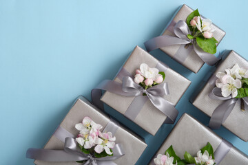 Gray gift boxes with apple flowers and silver ribbons on light blue background. Horizontal, space...