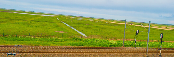 Railroad track in a green field in wetland below a blue cloudy sky in springtime, Almere,...