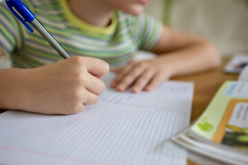 Close-up of a little girl's hand doing homework using textbooks, a workbook and a pencil. The idea...