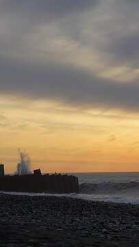 Wave hit large metal fence and rose high into air at sunset. Tsunami hits shore. Strong storm, wind and high big waves. vertical video