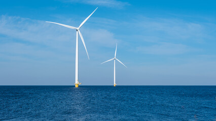 Two majestic wind turbines stand tall in the vast ocean, capturing the power of the wind and...