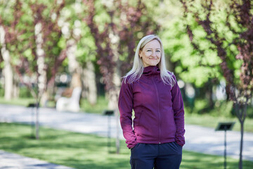 A middle-aged woman smiles confidently in a park, dressed in sportswear, ready for her morning run