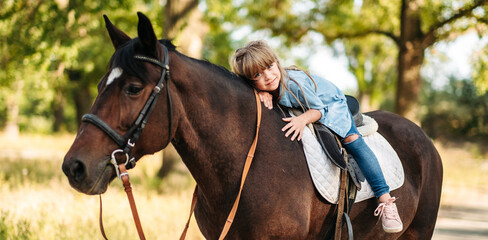 Cute little girl with long hair riding a horse outdoors. Pet therapy
