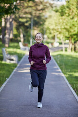 Joyful middle-aged woman runs through a park, her smile radiating health and vitality