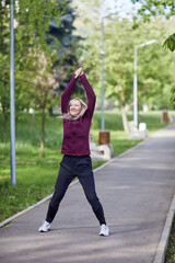 Mature woman stretching arms up in joy while exercising in a sunny park