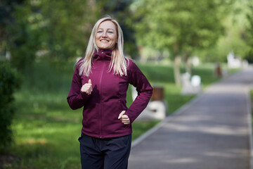 Joyful middle-aged woman jogging through a lush park, exuding happiness