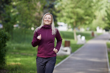 Smiling middle-aged woman running through a vibrant park