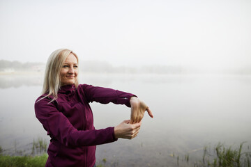 Mature woman stretching outdoors, exuding confidence against a foggy lakeside backdrop - Powered by Adobe