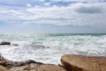 Fototapeta na wymiar travel, sea wave on rocks against cloudy sky, sea coast with waves, waves on the beach, natural background texture of sea sky and stones