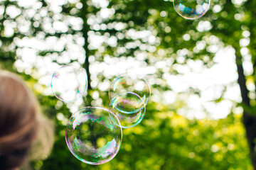 child playing with flying soap bubbles, festive atmosphere, sun rays, greenery, fun