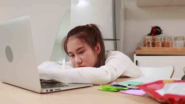 Tired exhausted, fatigue and fell asleep. Yaoung asian thai female working on laptop in kitchen room at home. Overwork. Exhausted woman  sleeply eye at workplace