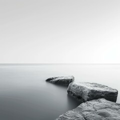 Black and white photo of large rocks in the middle of a calm lake with a clear sky in the background