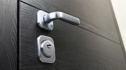 Close-up of a metallic handle and a keyhole of a black entrance door