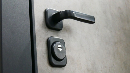 Close-up of a black handle and a keyhole of a gray front door