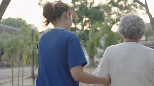 Young nurse and elderly asian senior woman on wheelchair, Asian careful caregiver and patient,  Nurse gives a pep talk to an elderly female patient in the garden in the evening. Health insurance.