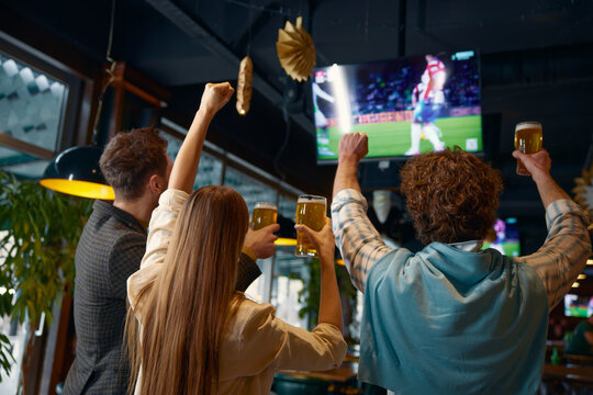 Happy excited group of friends watching football match on tv in pub