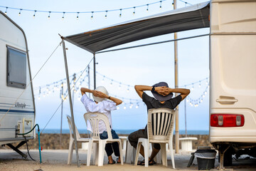 Couple of van life camper sitting by the caravan at seaside campsite for off grid living for...