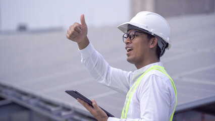 An engineer in safety gear uses a digital tablet to inspect and manage solar panels installed on the roof of an industrial building.
