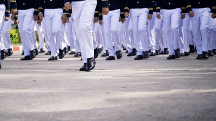 A group of military personnel march in synchrony, wearing pristine white uniforms and black boots, during a formal parade ceremony.
