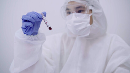 Close-up of a scientist in full protective suit and gloves holding a blood sample for analysis in a sterile laboratory environment.
