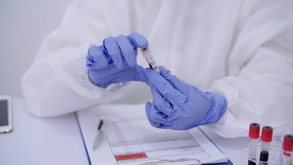 A scientist, dressed in full protective gear, carefully examines a blood sample tube in a modern laboratory setting to ensure accurate results.
