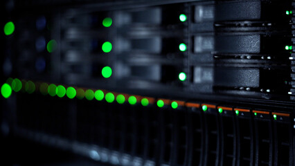 Close-up image capturing the details of a data center's active network servers, highlighted by the blinking green lights indicating operation status.
