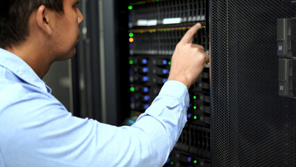 An IT professional in a blue shirt manages and monitors network servers in a data center, ensuring system stability and security.
