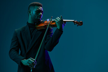 Fototapeta premium Elegant man in black suit performing on violin against vibrant blue background in studio setting