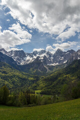 Obraz premium The mighty mountains covered in thin snow over the green spring forrest in the valley.