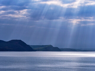 Looking across Lyme Bay towards the jurassic coastline on a spring morning with crepuscular rays shining through dark stormy clouds
