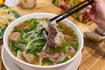 Enjoying Vietnamese Beef Pho: A Close-up of Tender Beef and Noodles Being Lifted with Chopsticks
