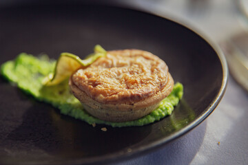 Exquisite Miniature Savory Pie or Tart on a Bed of Lush Green Pea Purée, Presented on a Sleek Dark Plate