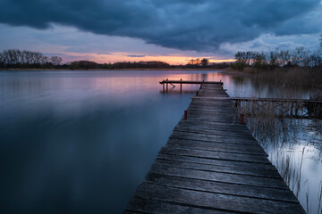Naklejka premium Wooden pier on the lake at cloudy sunset, view on a spring evening