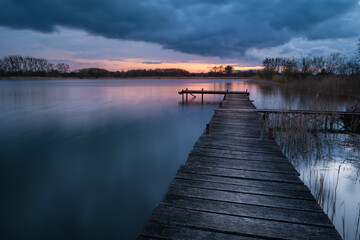 Wooden pier on the lake at cloudy sunset, view on a spring evening