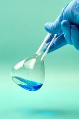 Hand of unrecognizable researcher in latex glove holding titration flask of blue chemical substance during experiment in laboratory