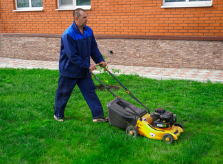 The man is working in the garden. Mowing grass with a lawn mower.