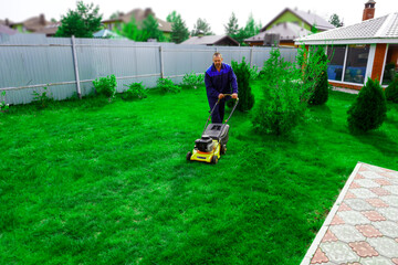 The man is working in the garden. Mowing grass with a lawn mower.