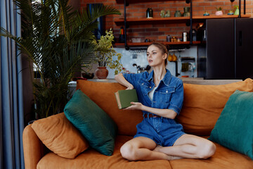 Obraz premium Young woman enjoying a peaceful moment on a cozy orange couch with a book and coffee cup