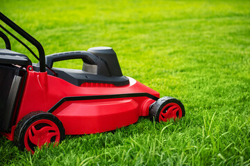 The process of mowing the lawn with a lawnmower. Red and black lawnmower on green grass.