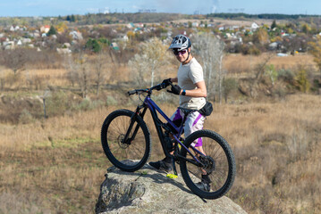 Obraz premium A mountain biker stands on a rock near a cliff.