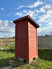 A rustic toilet made of red boards in a clearing